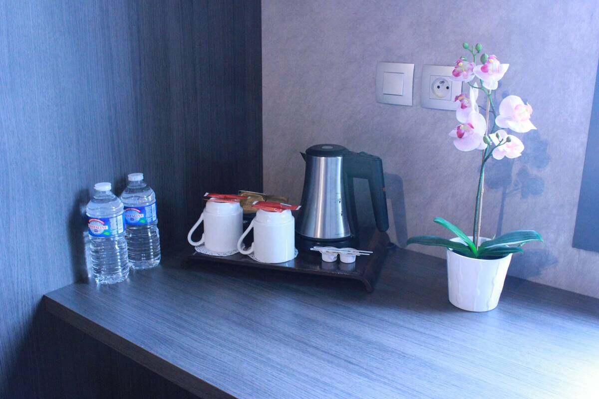 Habitación de hotel con un escritorio de madera, dos botellas de agua, una cafetera y una orquídea en maceta.