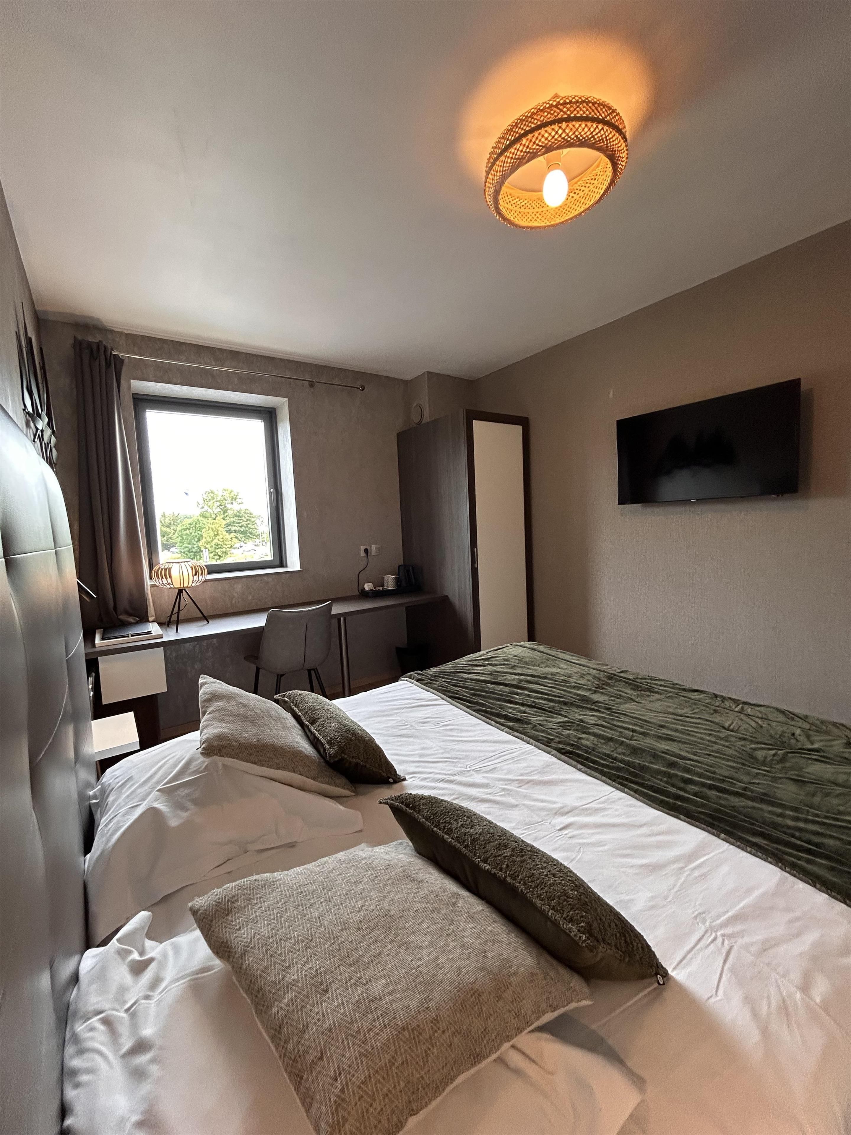 A hotel room with a bed, a desk, a chair, a television, and a window.