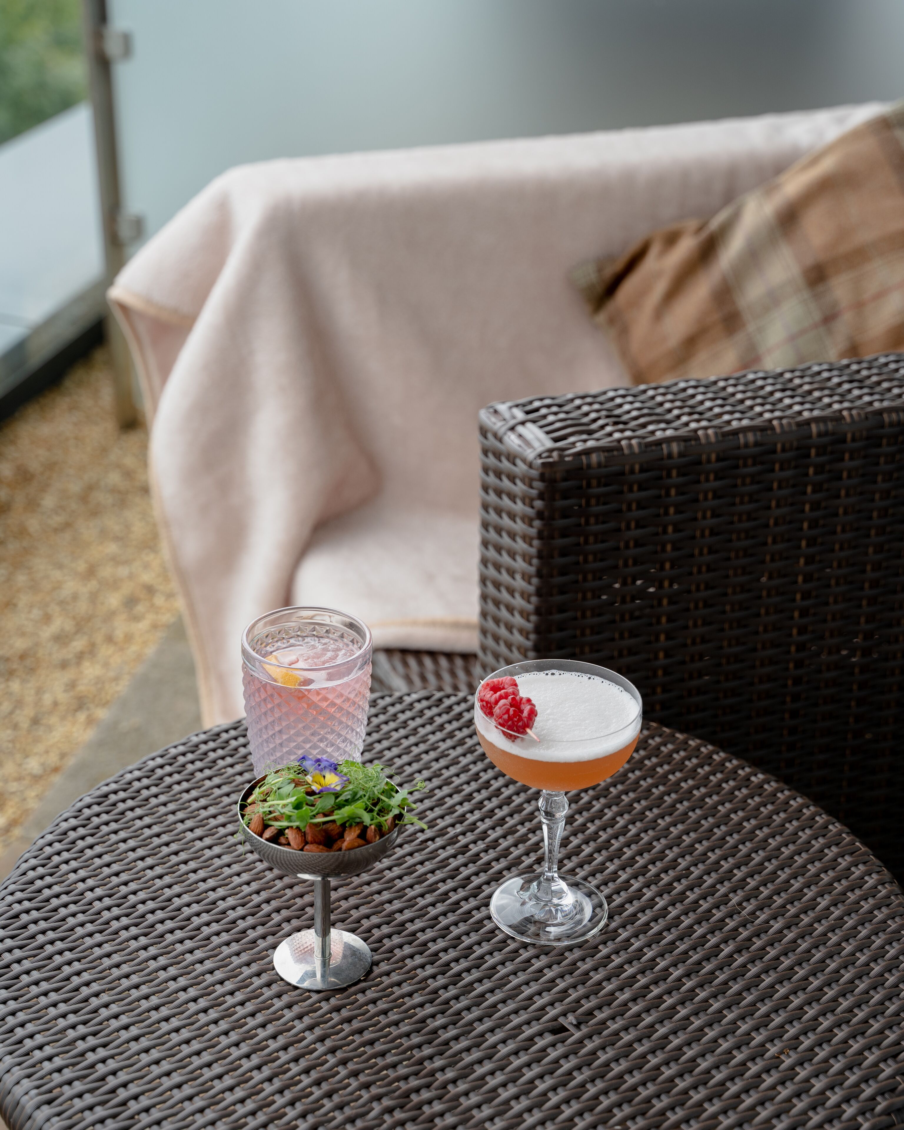 A wicker table with two drinks and a small salad bowl.