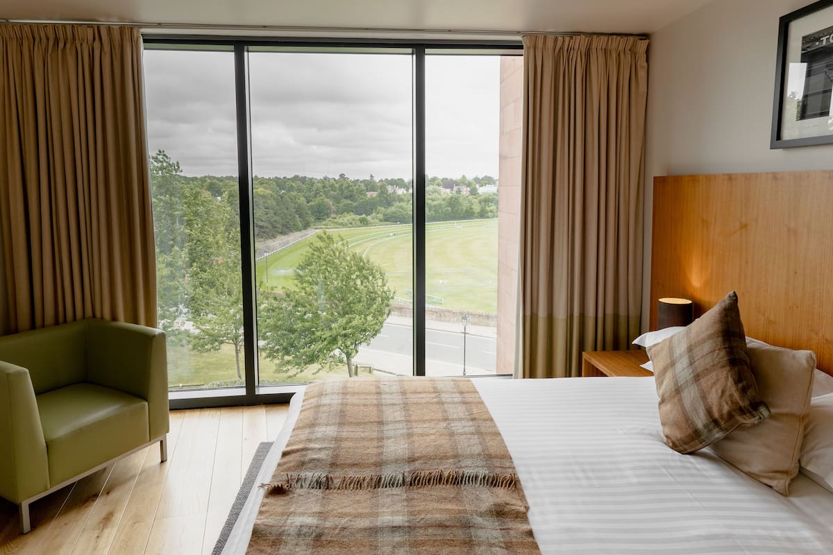 A bedroom with a large window, a bed, a green armchair, and a nightstand.