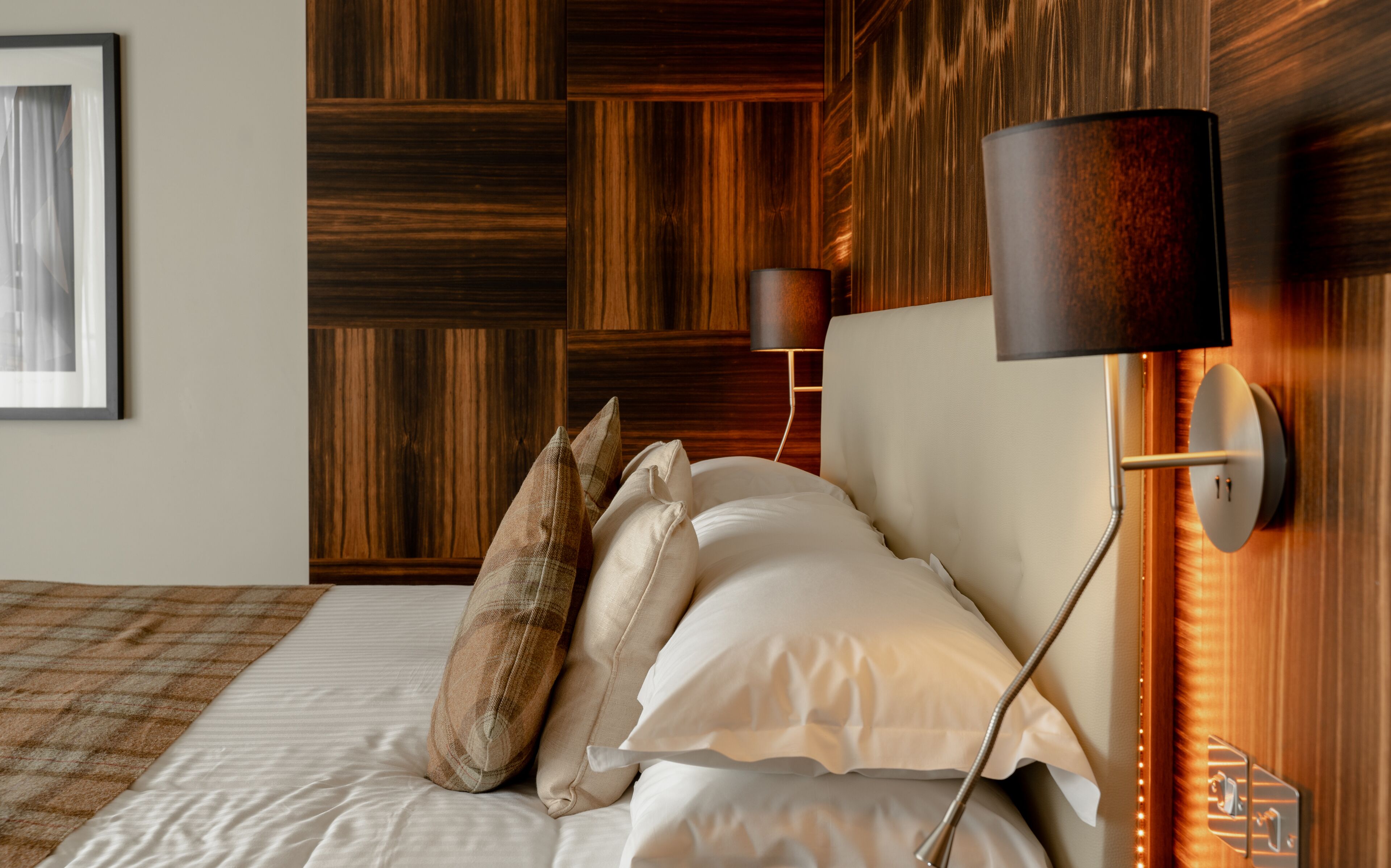 A neatly made bed with pillows, a wall-mounted lamp, and a wooden panel wall.