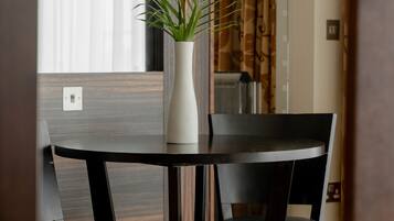 A dining area with a round table, two chairs, and a white vase with a plant.