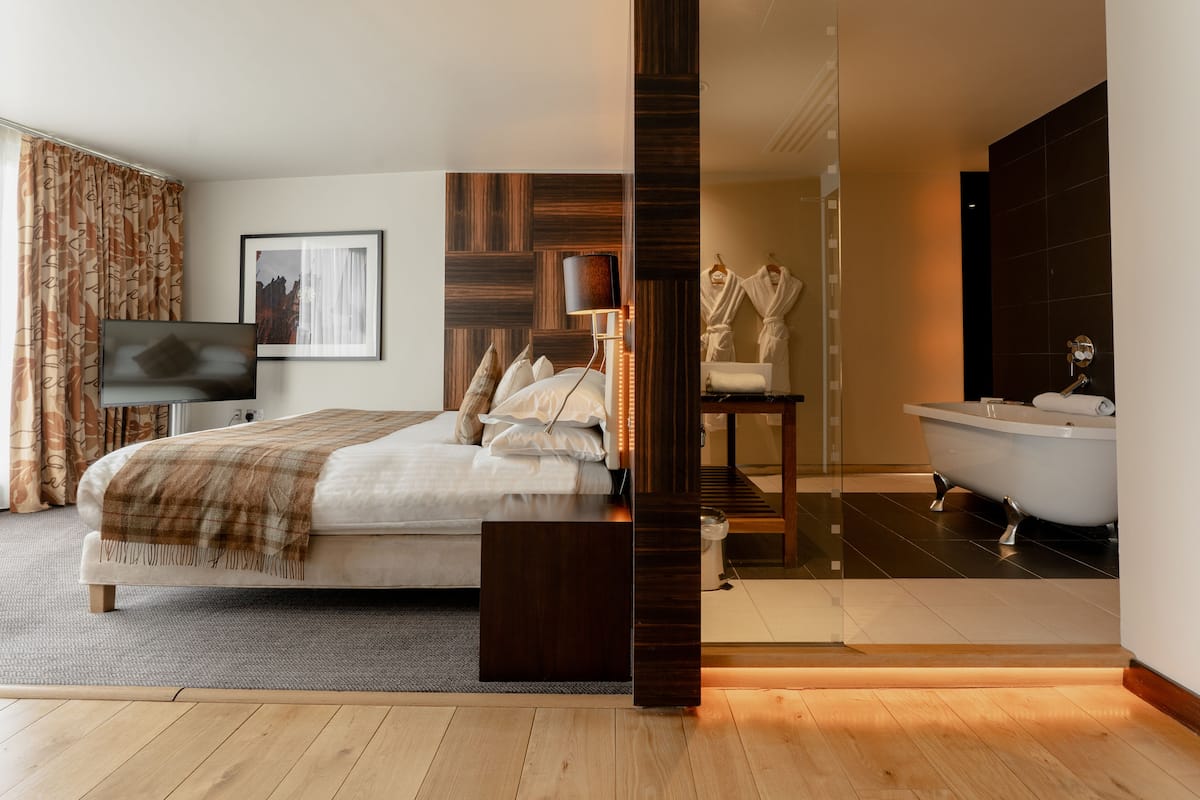 A modern bedroom with a bed, a TV, a bedside table, a mirror, a bathroom with a bathtub, and a shower.