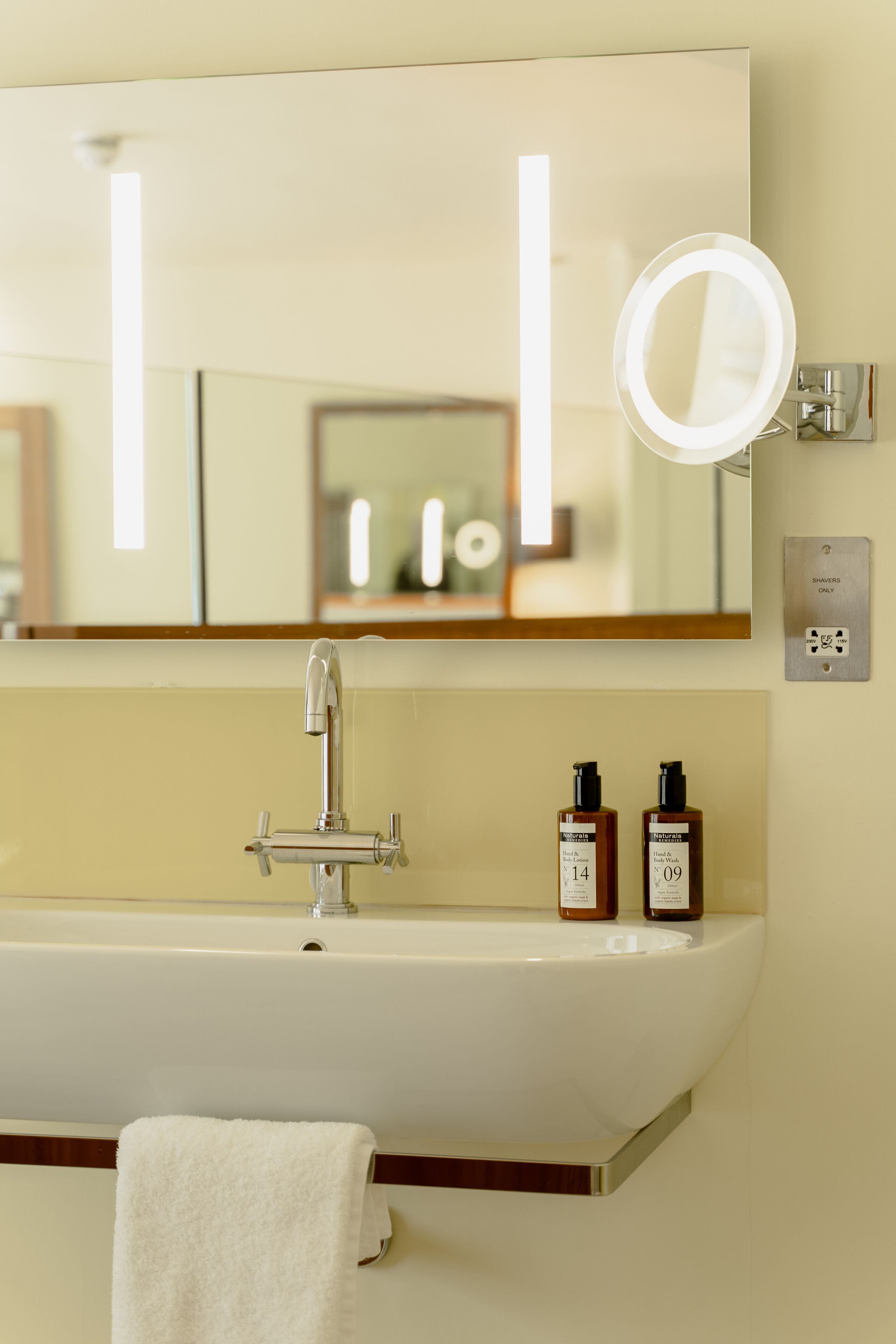 A bathroom with a large mirror, a sink, and two bottles of shampoo.