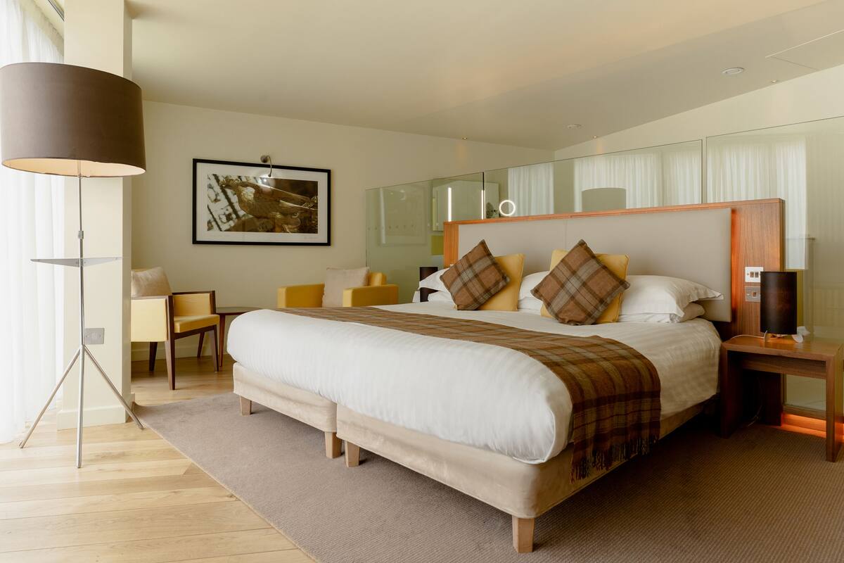 A modern hotel room with a large bed, a bedside table, a lamp, and a chair.