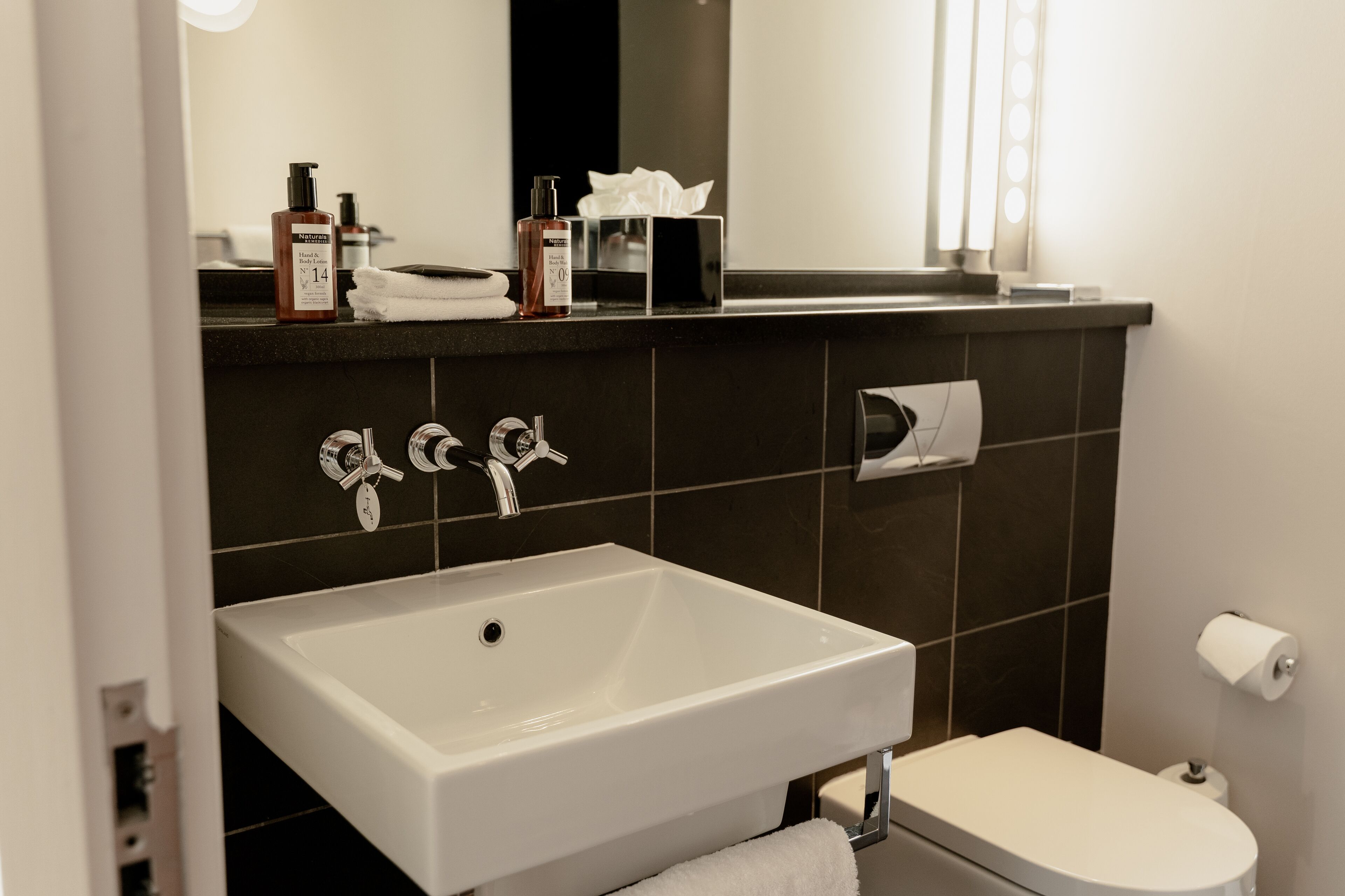 Un baño moderno con un lavamanos blanco, dos grifos, un espejo y un inodoro.