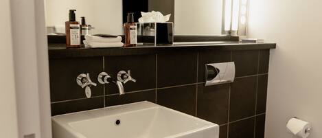 Un baño moderno con un lavamanos blanco, dos grifos, un espejo y un inodoro.