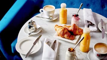 Un desayuno con croissants, jugo de naranja, café y un frasco de mermelada sobre una mesa de mármol.
