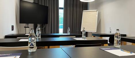 A conference room with a large flat-screen TV, a whiteboard, and tables with water bottles and notepads.