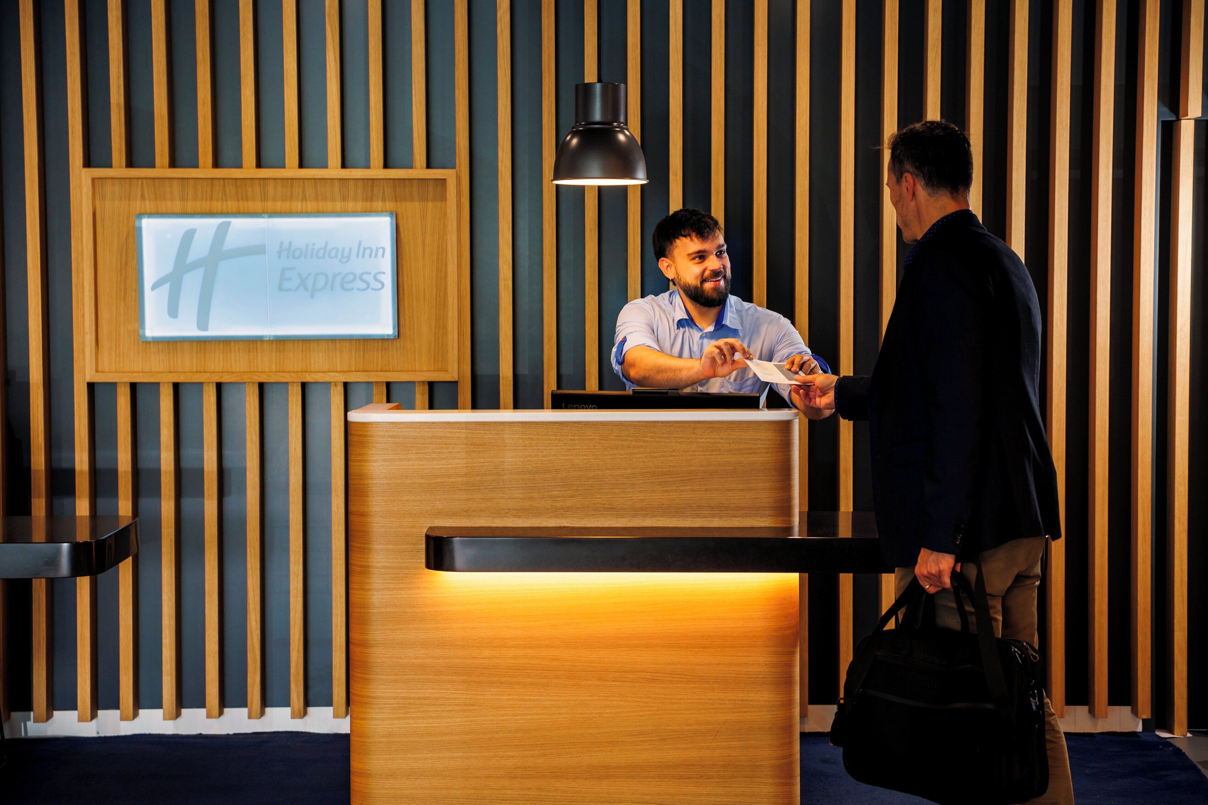 A reception desk at a Holiday Inn Express with a modern design, a framed sign, and a black pendant light.