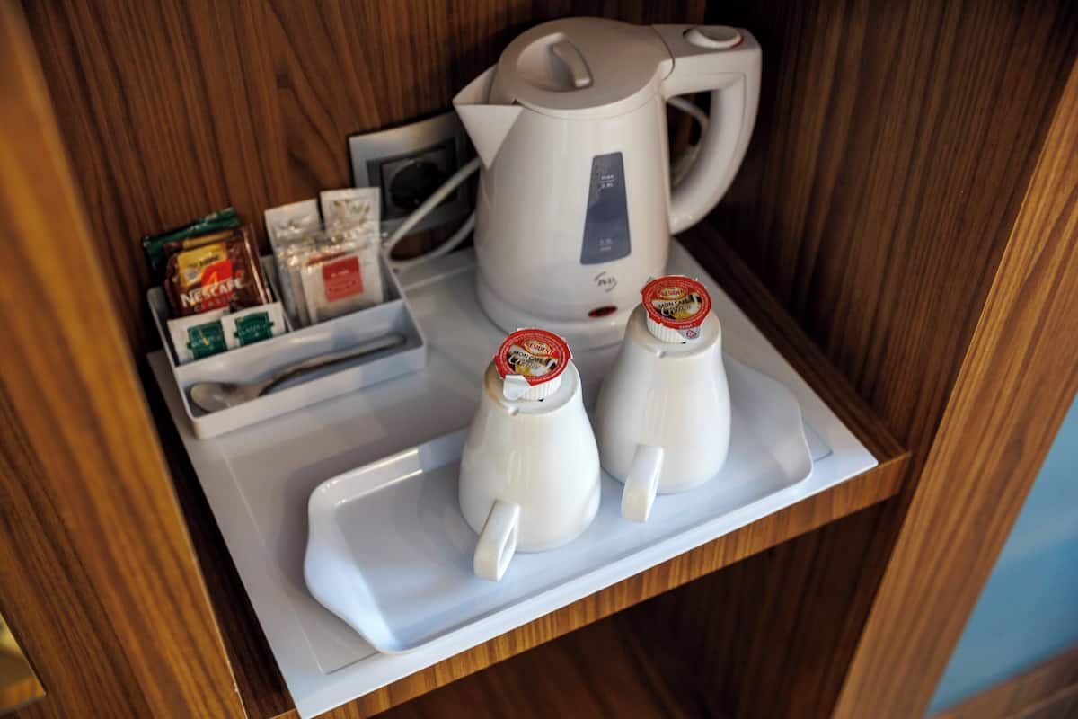 A tray with a white electric kettle, two small white containers with red lids, and some packaged food items.