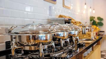 Una barra de buffet con varios recipientes de acero inoxidable, un backsplash de azulejos y una planta al fondo.