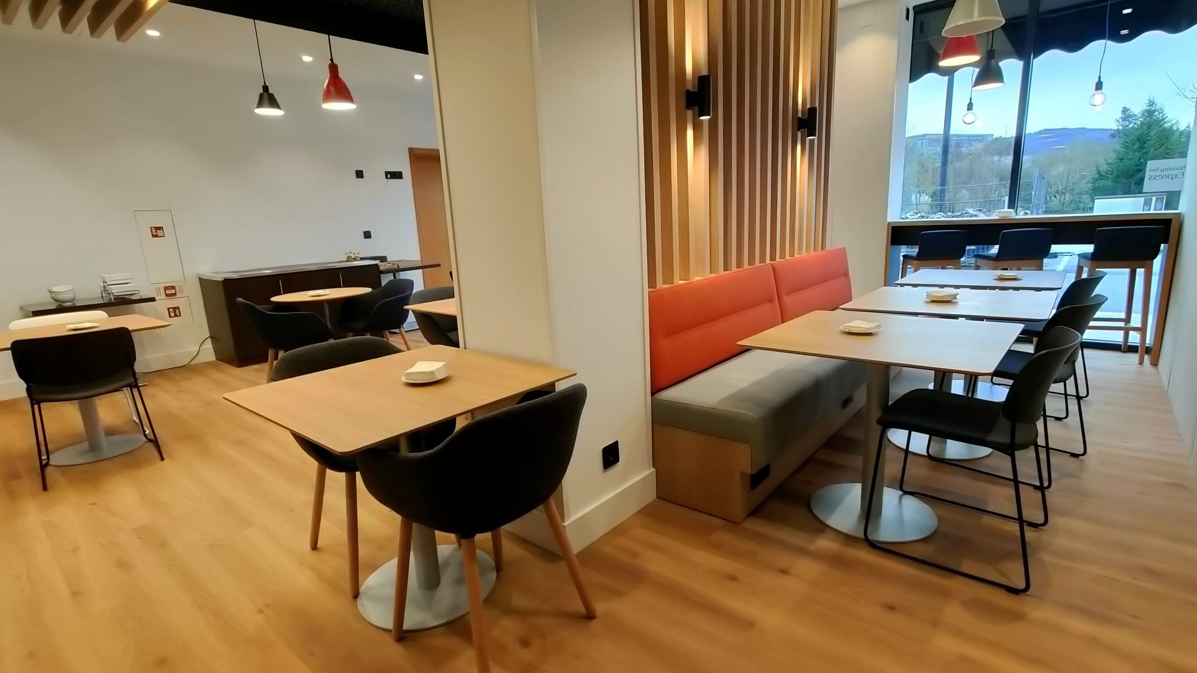 A modern cafe with wooden tables and black chairs, a red cushioned bench, and pendant lighting.
