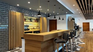 Un área de bar moderna con mostrador de madera, taburetes y pared de ladrillo de fondo.
