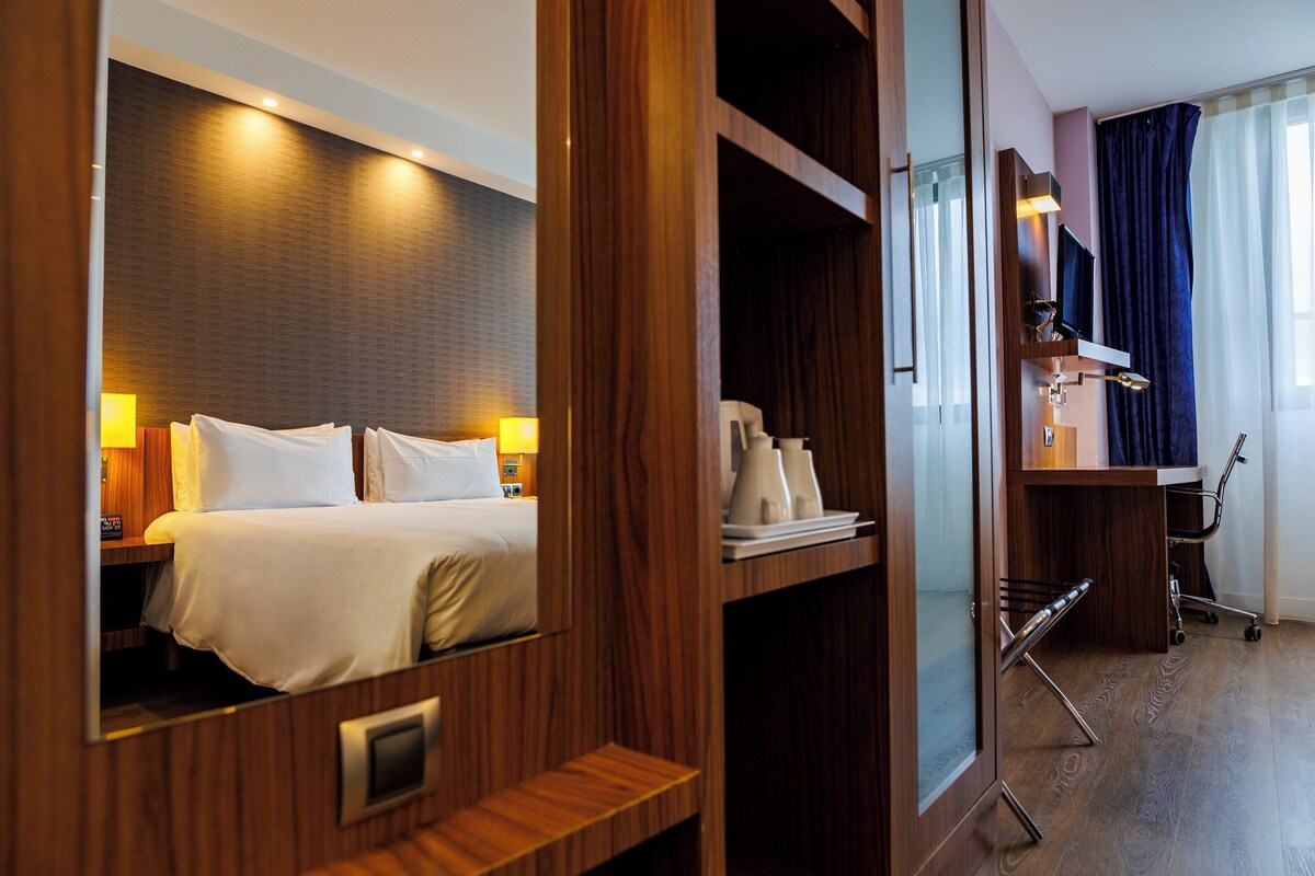 A hotel room with a bed, bedside lamps, a desk, and a chair.