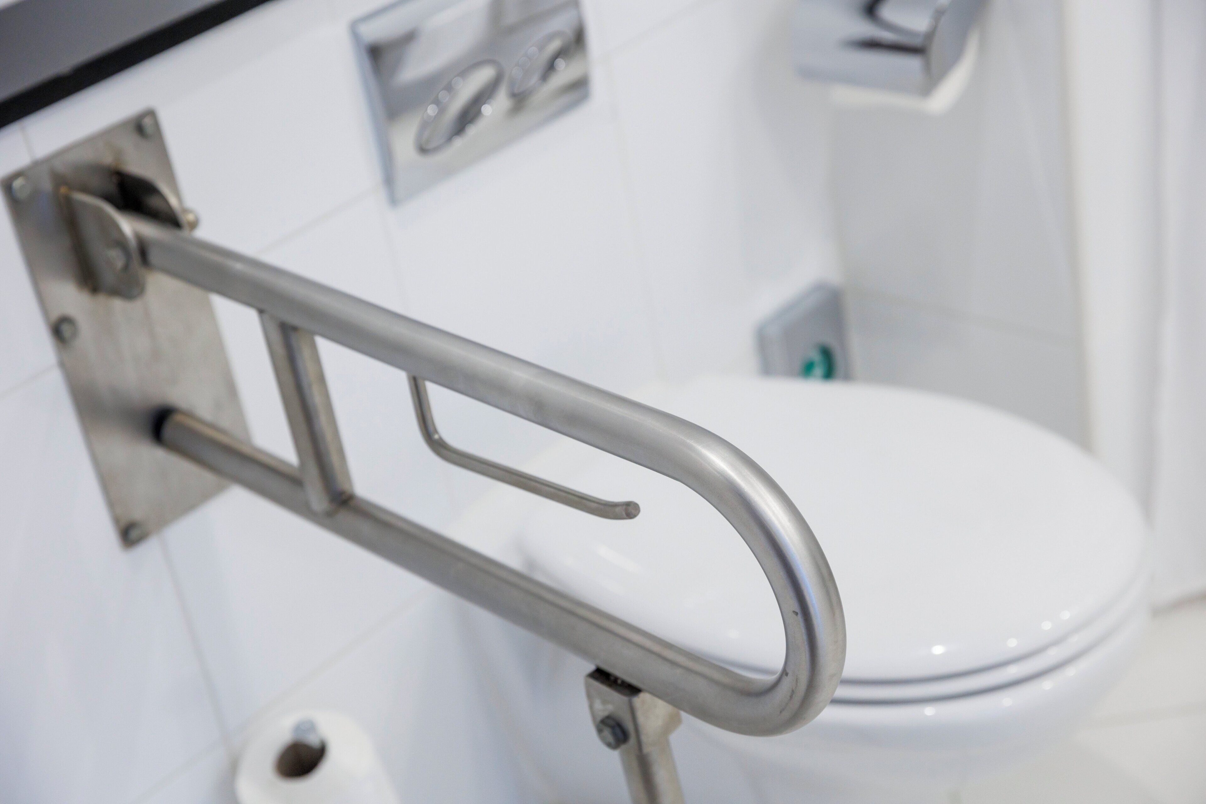 A bathroom with a white toilet, a metal grab bar, and a white tiled wall.