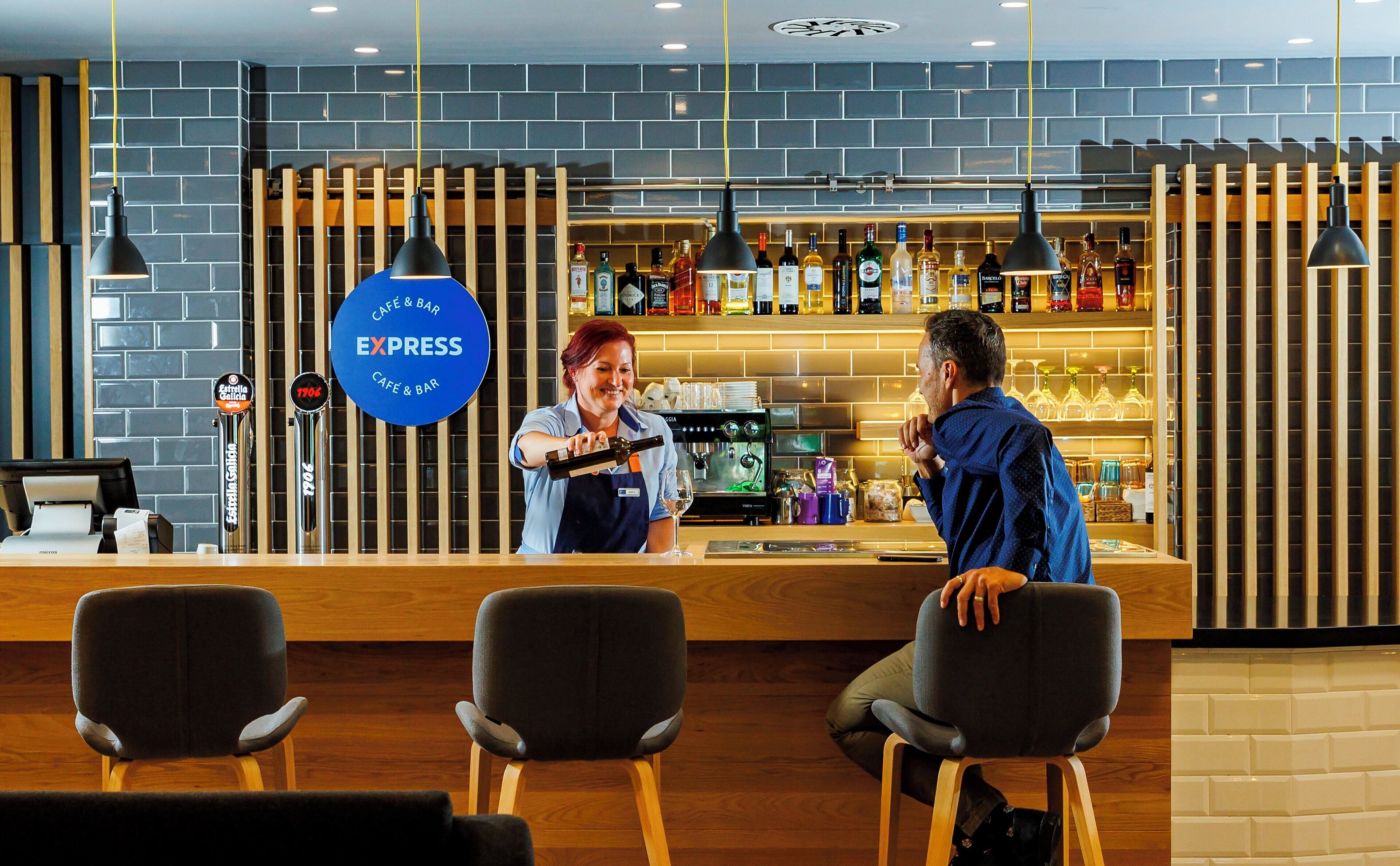 Een bar met een toonbank, barkrukken, een koffieapparaat en diverse flessen op planken.