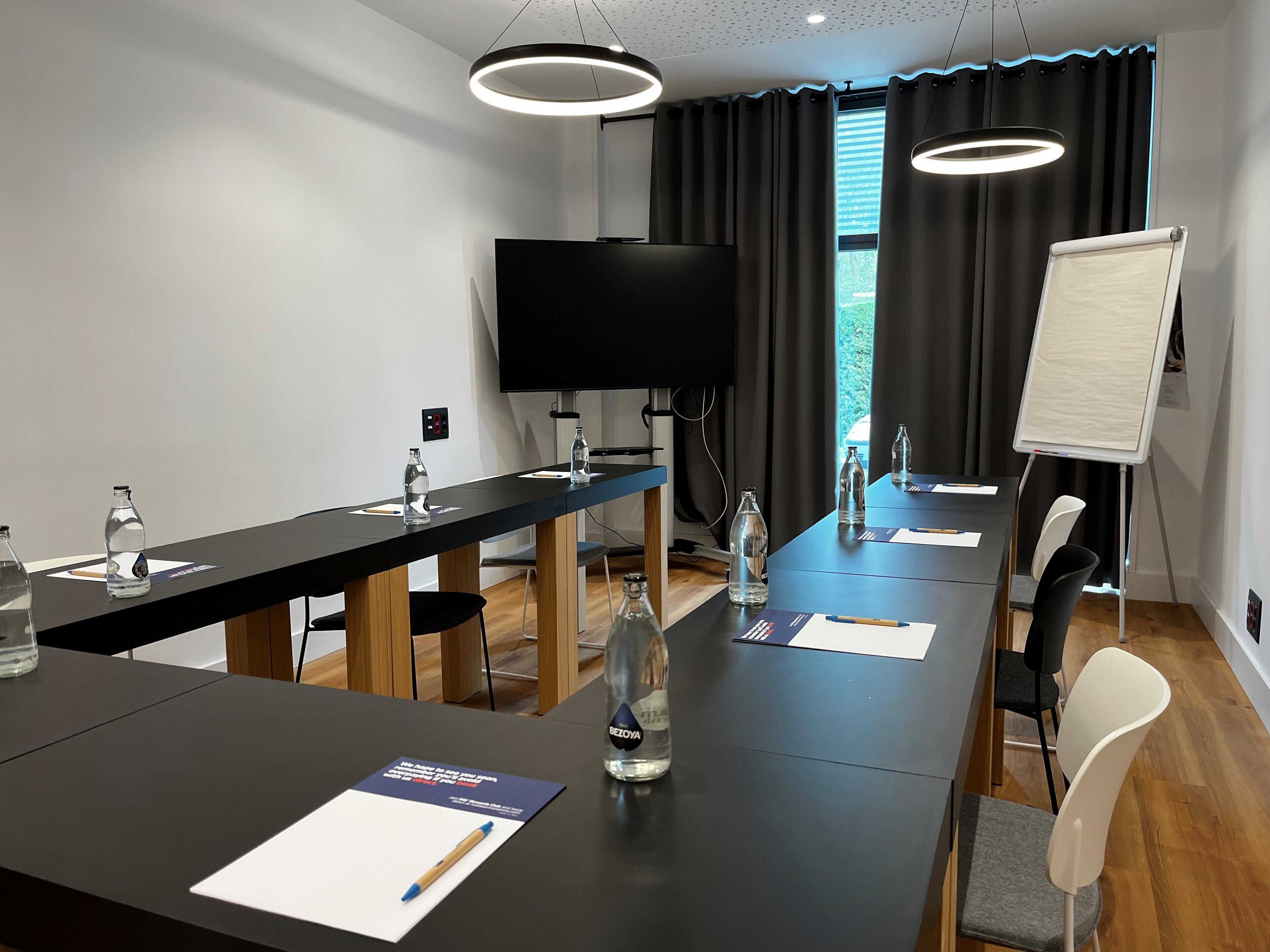 Un salón de conferencias con una mesa larga, sillas, una pizarra y un televisor.