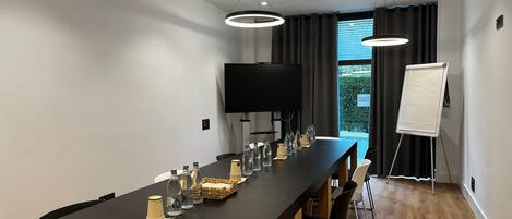 A modern conference room with a long table, chairs, a TV, and a whiteboard.