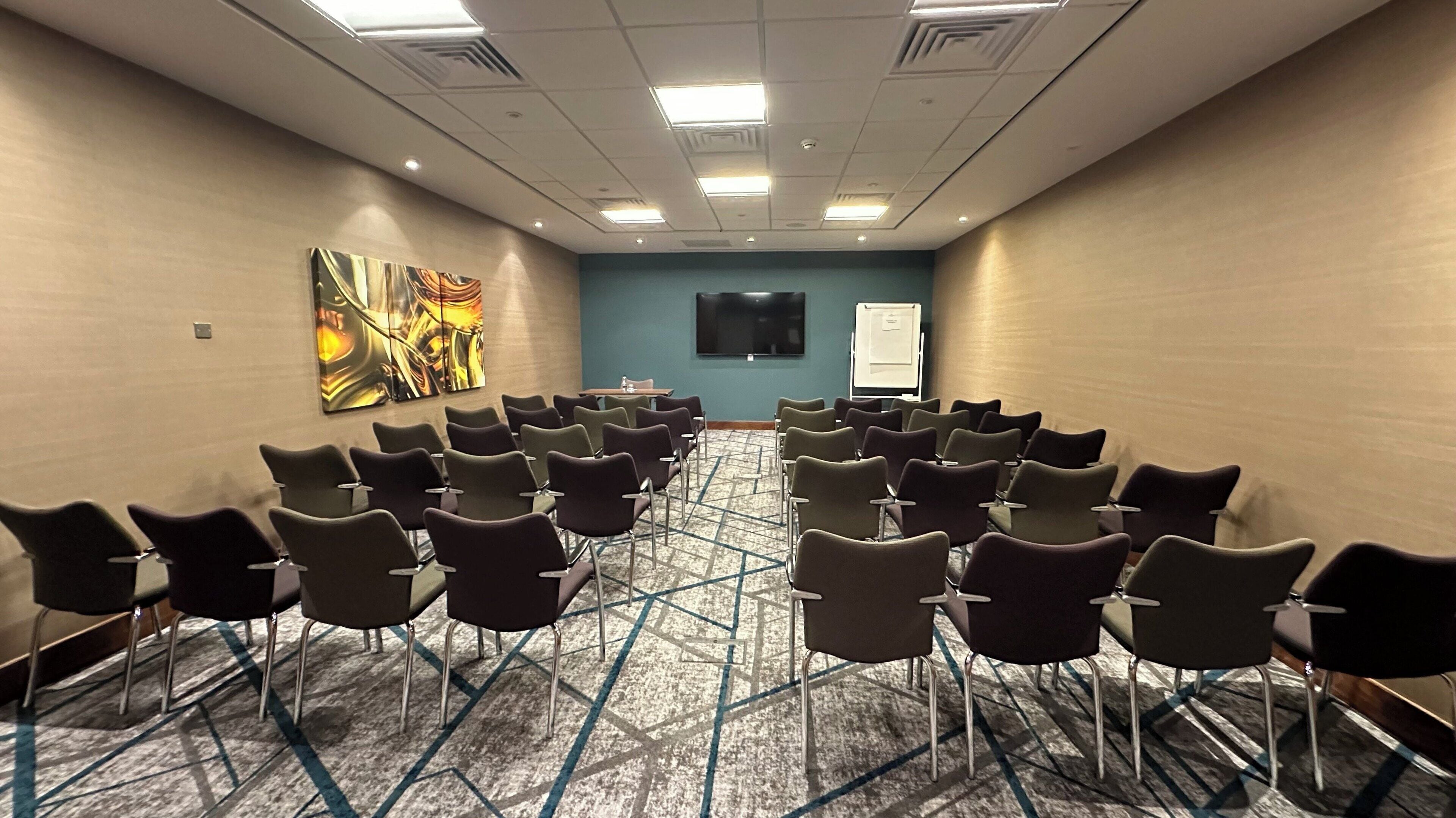 A conference room with rows of chairs, a large abstract painting on the wall, a whiteboard, and a flat-screen TV.