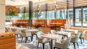 A modern restaurant with wooden tables and chairs, large windows, and a view of greenery outside. - Crowne Plaza Reading by IHG (Reading)