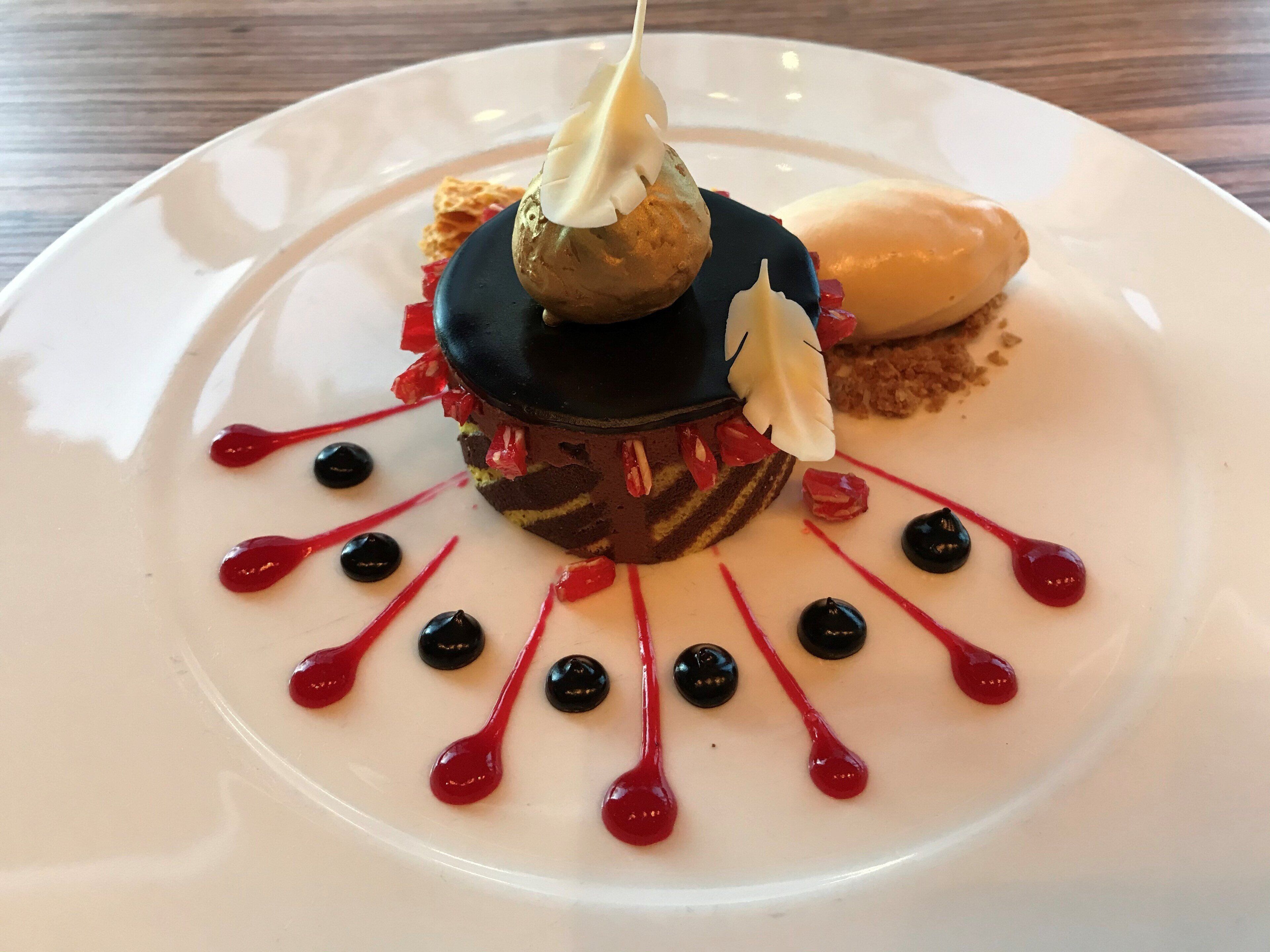 Postre sobre un plato blanco con delicados chorros de salsa roja y negra.