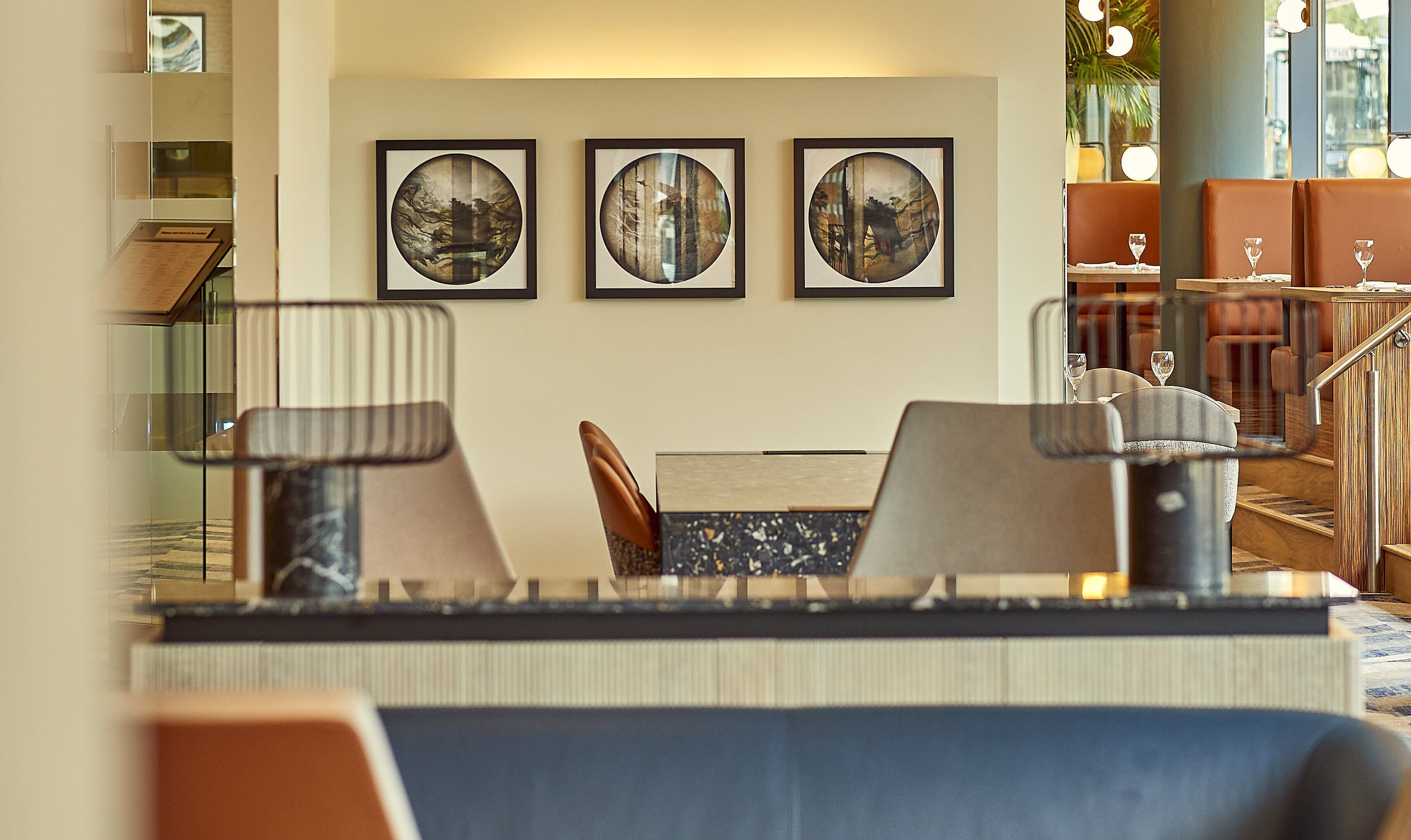 A dining area with a table set for two, a staircase, and three framed artworks on the wall.