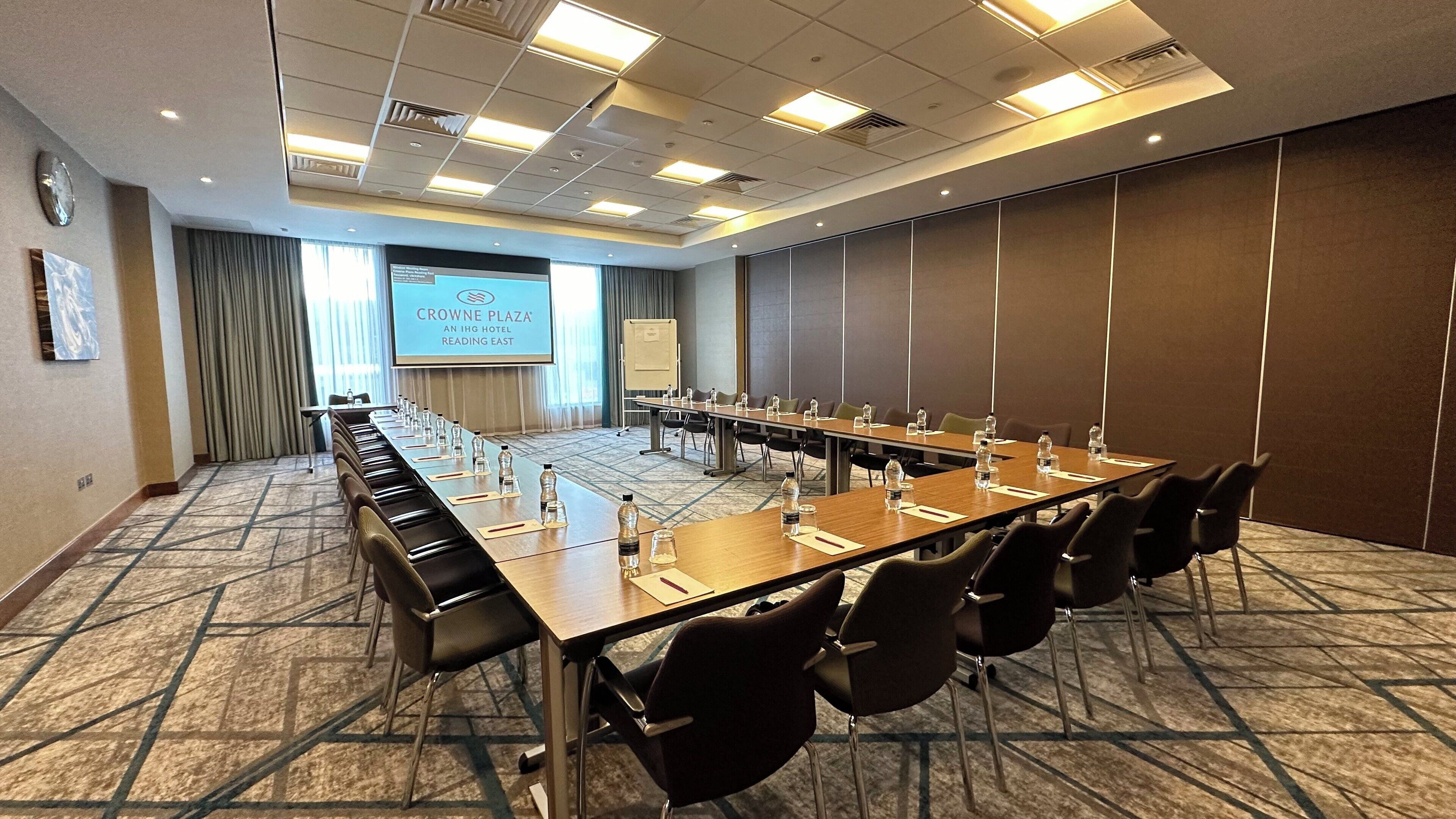 A conference room with a long table, chairs, a projector screen, and a presentation screen.