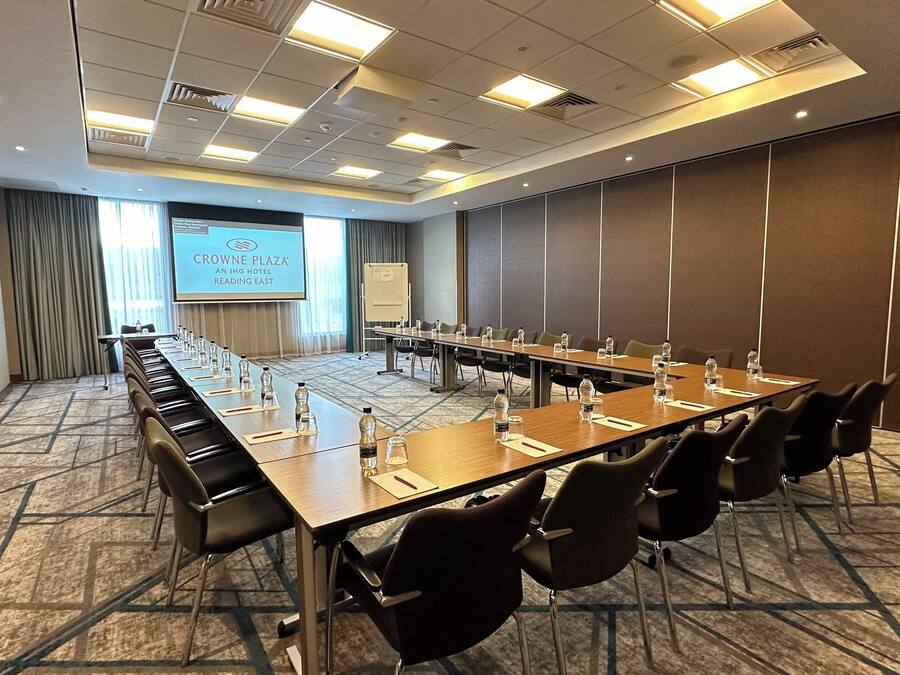A conference room with a long table, chairs, a projector screen, and a presentation screen.