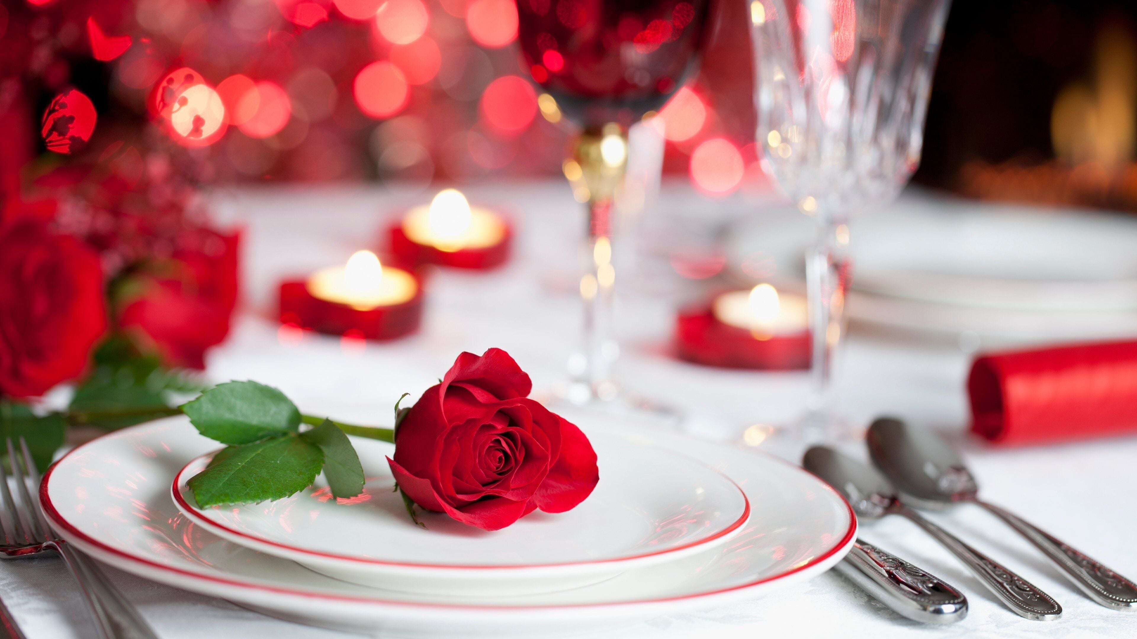 A dining table with a white plate, a red rose, and silverware.