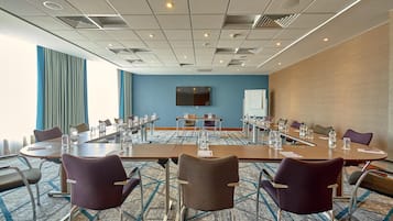Un salón de conferencias con una larga mesa, varias sillas y un televisor de pantalla plana en la pared.