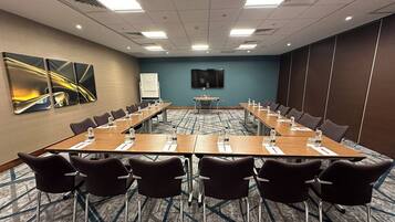 A conference room with a long table, chairs, a whiteboard, and a TV screen.