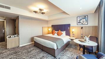 A hotel room with a large bed, bedside tables, a seating area with a table and chairs, and a painting on the wall.