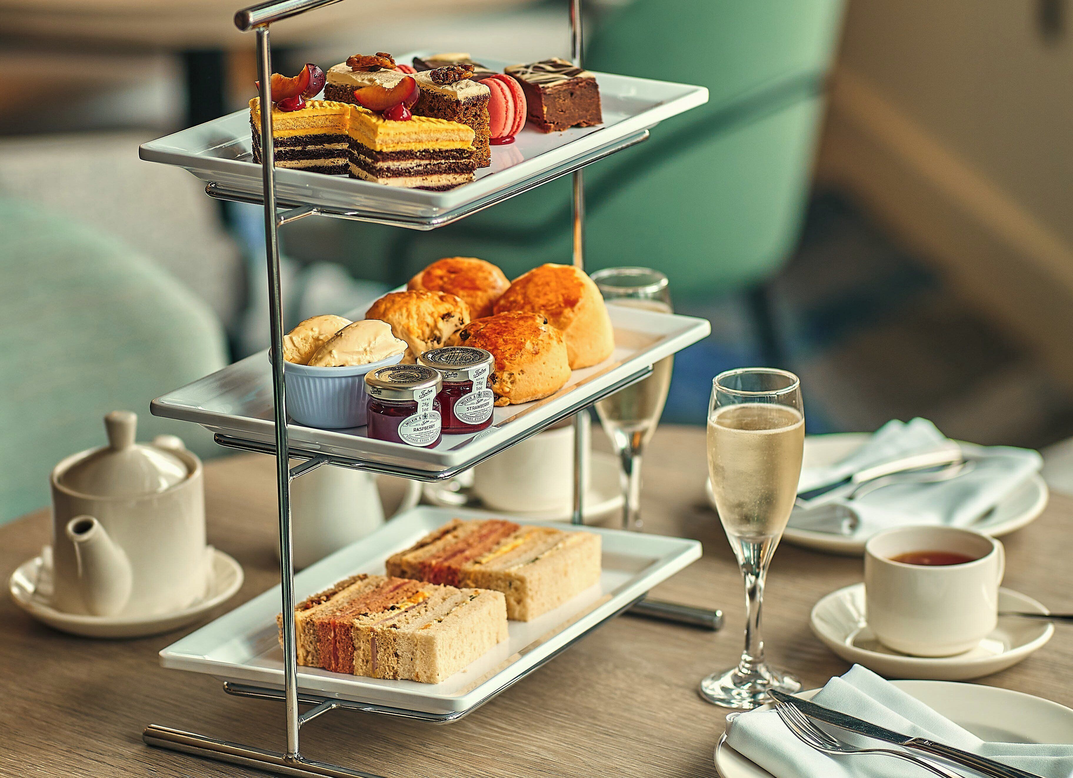 Un soporte de tres niveles con diversos pasteles y tartas, una copa de champán y una taza de té sobre una mesa.