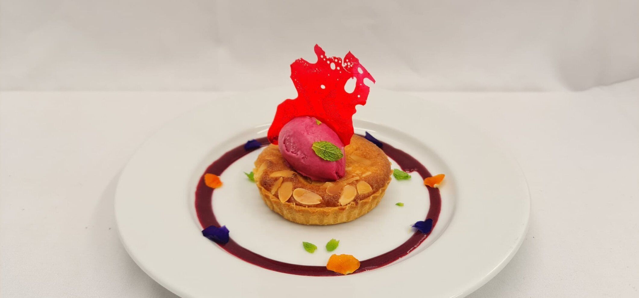 A dessert on a white plate with a red garnish and a berry on top.