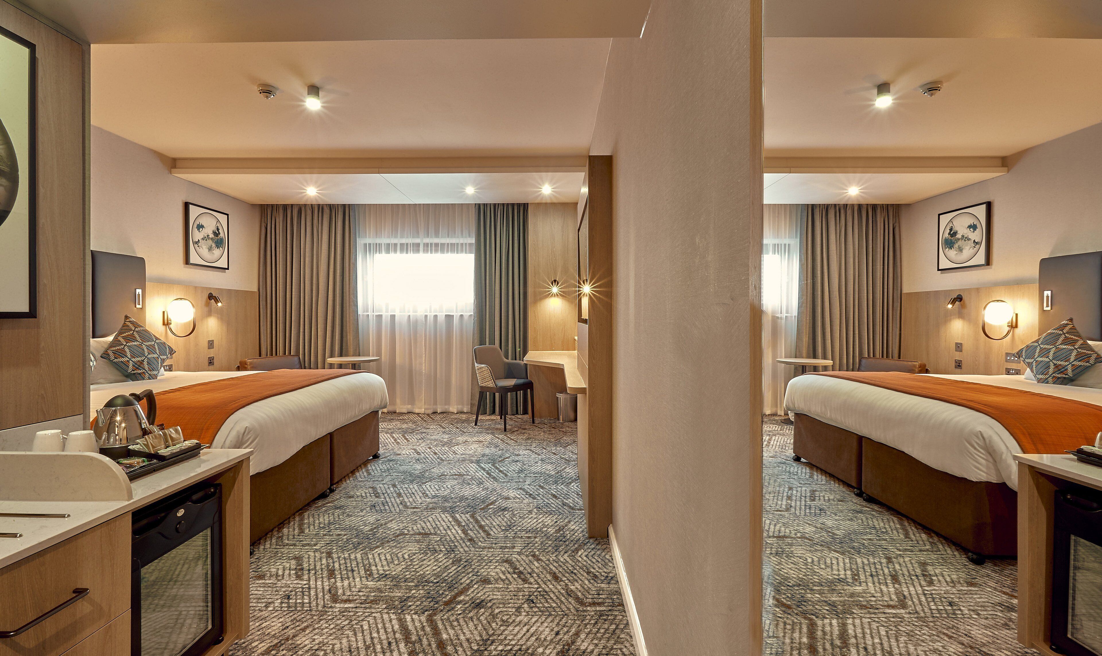 A hotel room with two beds, a desk, a chair, a small table, and a bathroom.