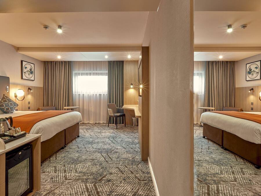 A hotel room with two beds, a desk, a chair, a small table, and a bathroom.
