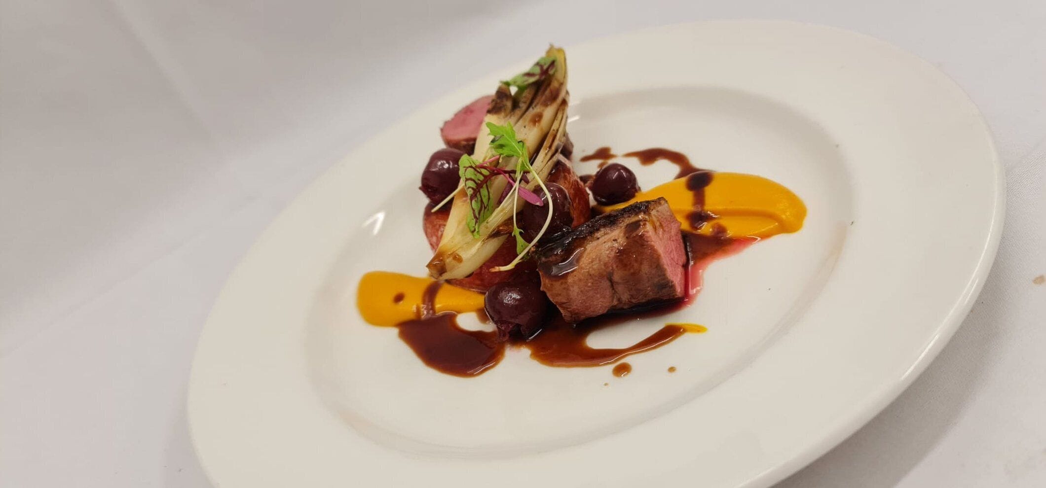 A white plate with a piece of meat, possibly steak, accompanied by some vegetables and a sauce.