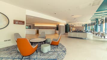 A hotel lobby with a reception desk, seating area with chairs, and a conference center.