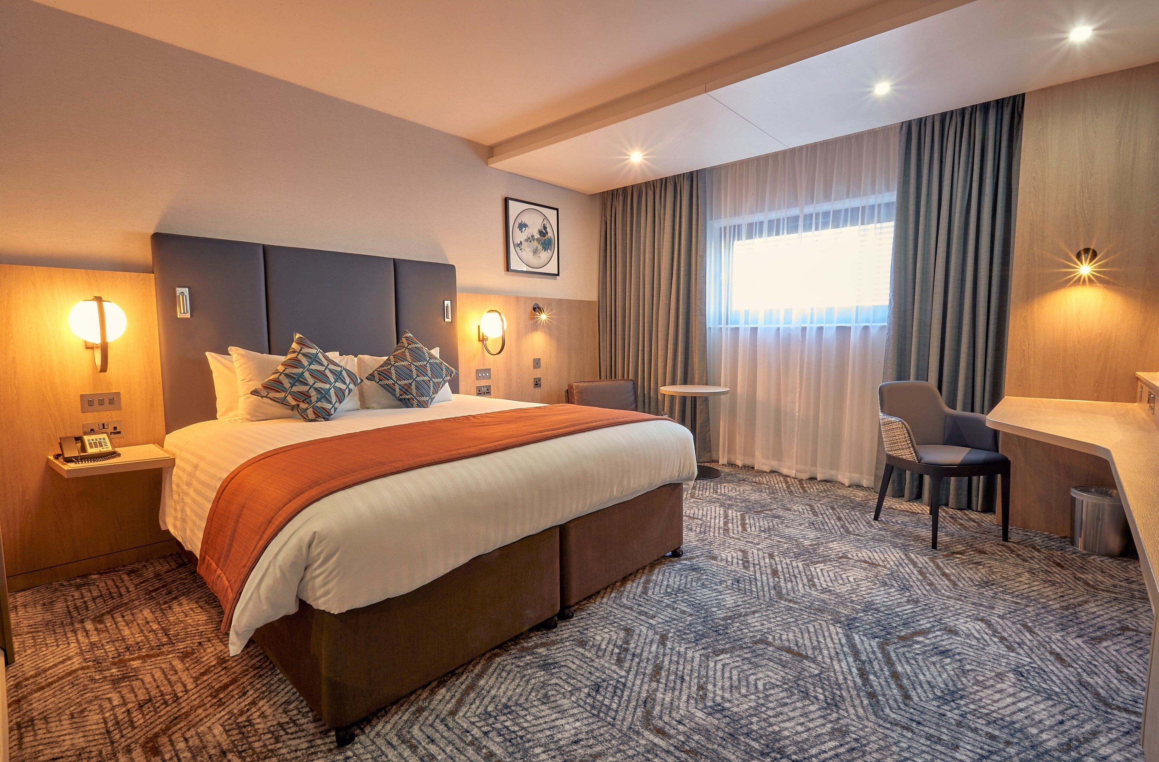 A hotel room with a large bed, bedside lamps, a desk, and a chair.
