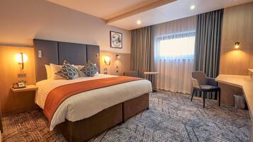 Una habitación de hotel con una cama grande, lámparas de noche, un escritorio y una silla.