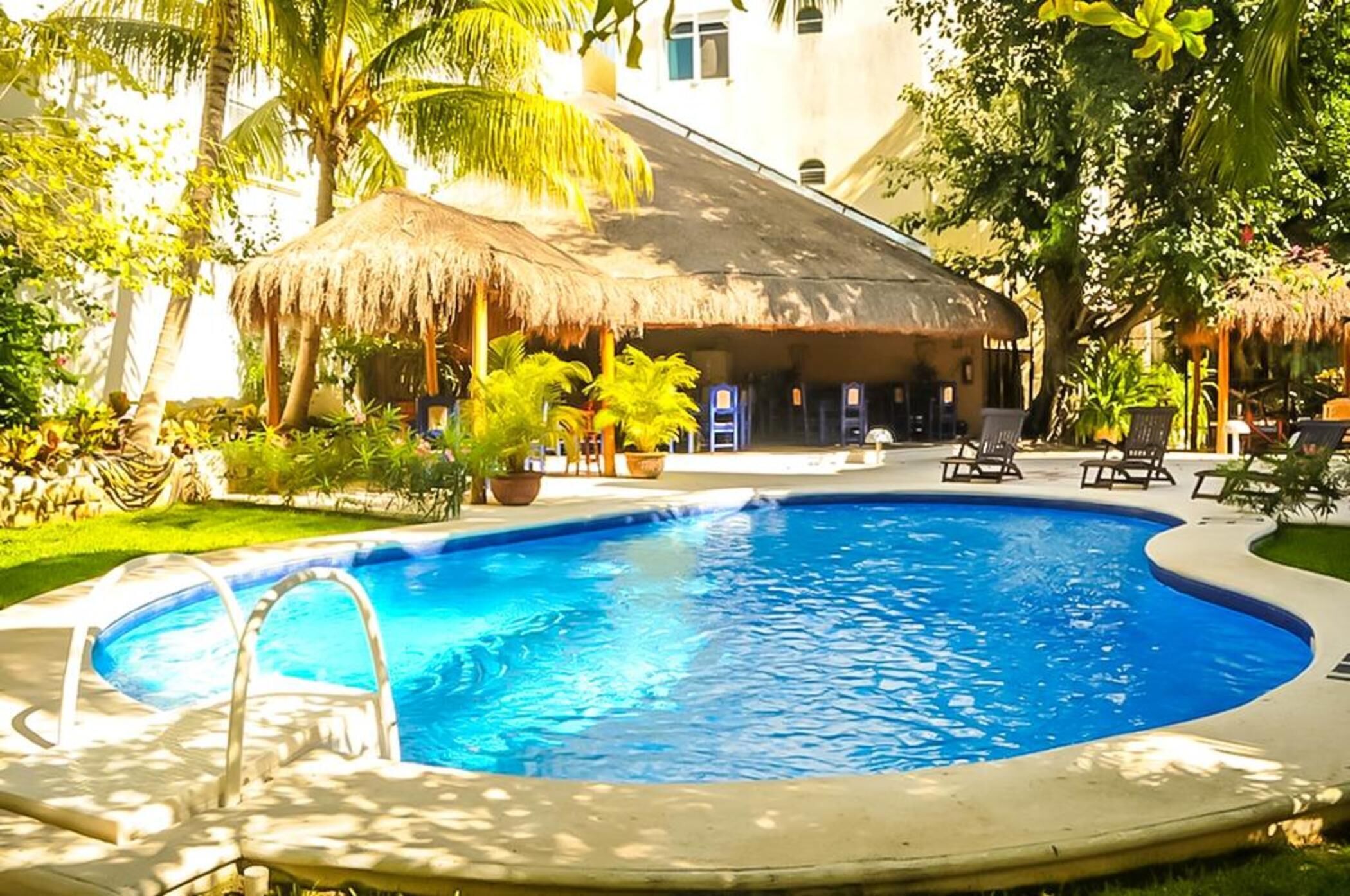 A swimming pool with a thatched-roof structure and lounge chairs in a tropical setting.