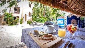 Un desayuno con una mesa, una taza de café, un vaso de zumo de naranja y un bol de fruta.