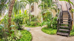 Un exuberante jardín interior con un sendero de concreto que conduce a una escalera de madera.