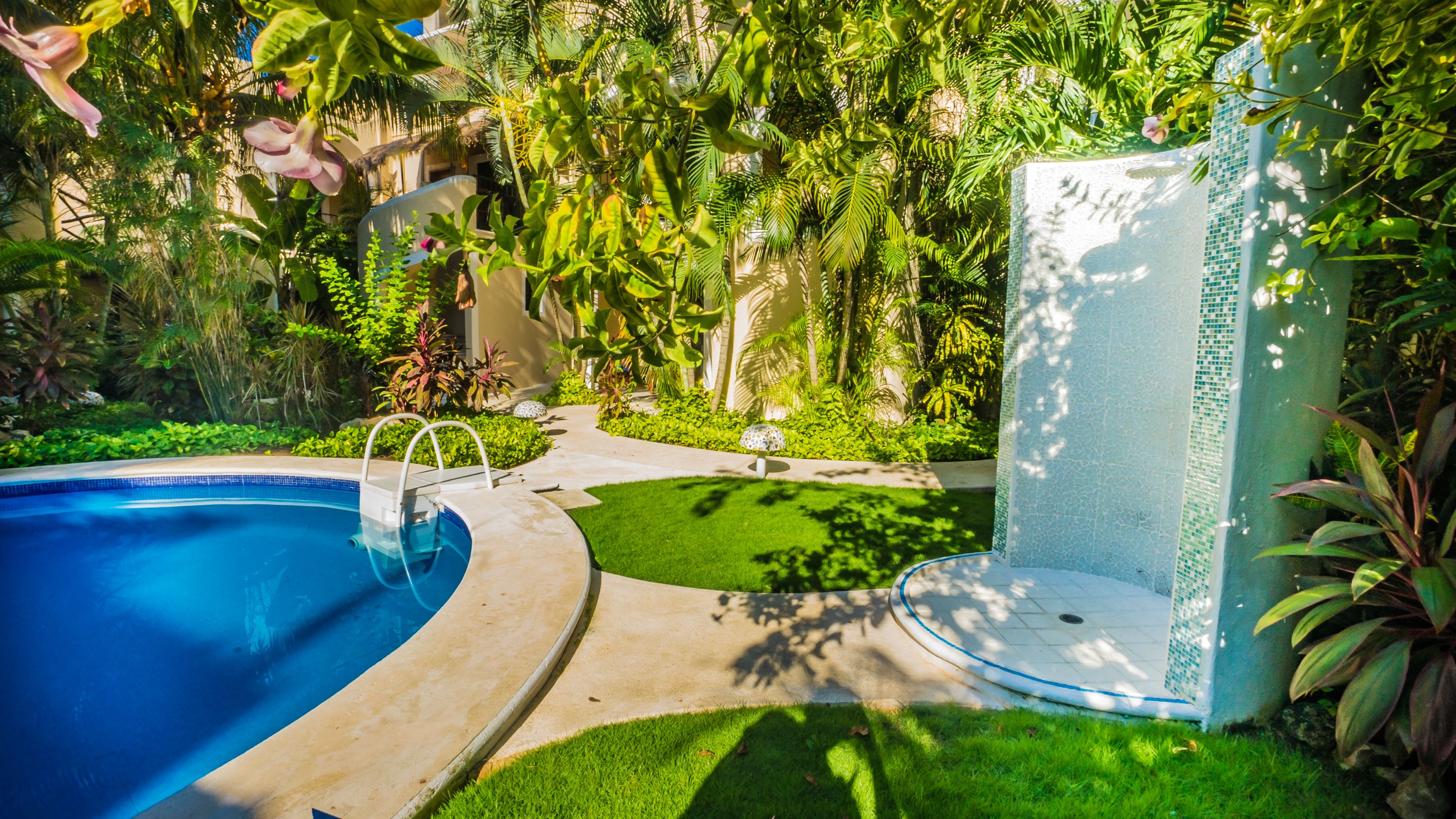A swimming pool with a curved edge, surrounded by lush greenery and a small lawn area.