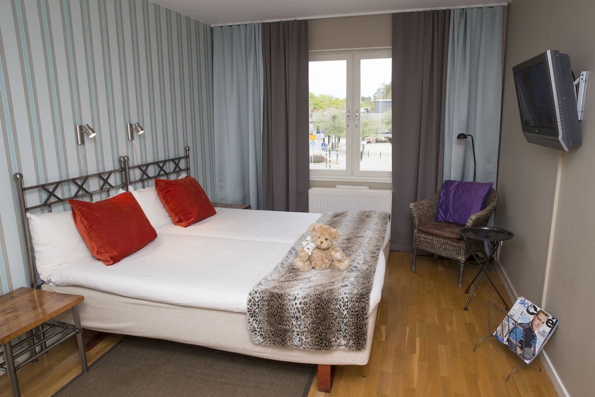 A hotel room with a bed, a chair, a table, a TV, and a window with curtains.