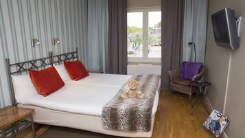 Habitación de hotel con cama, una silla, una mesa, televisor y ventana con cortinas.