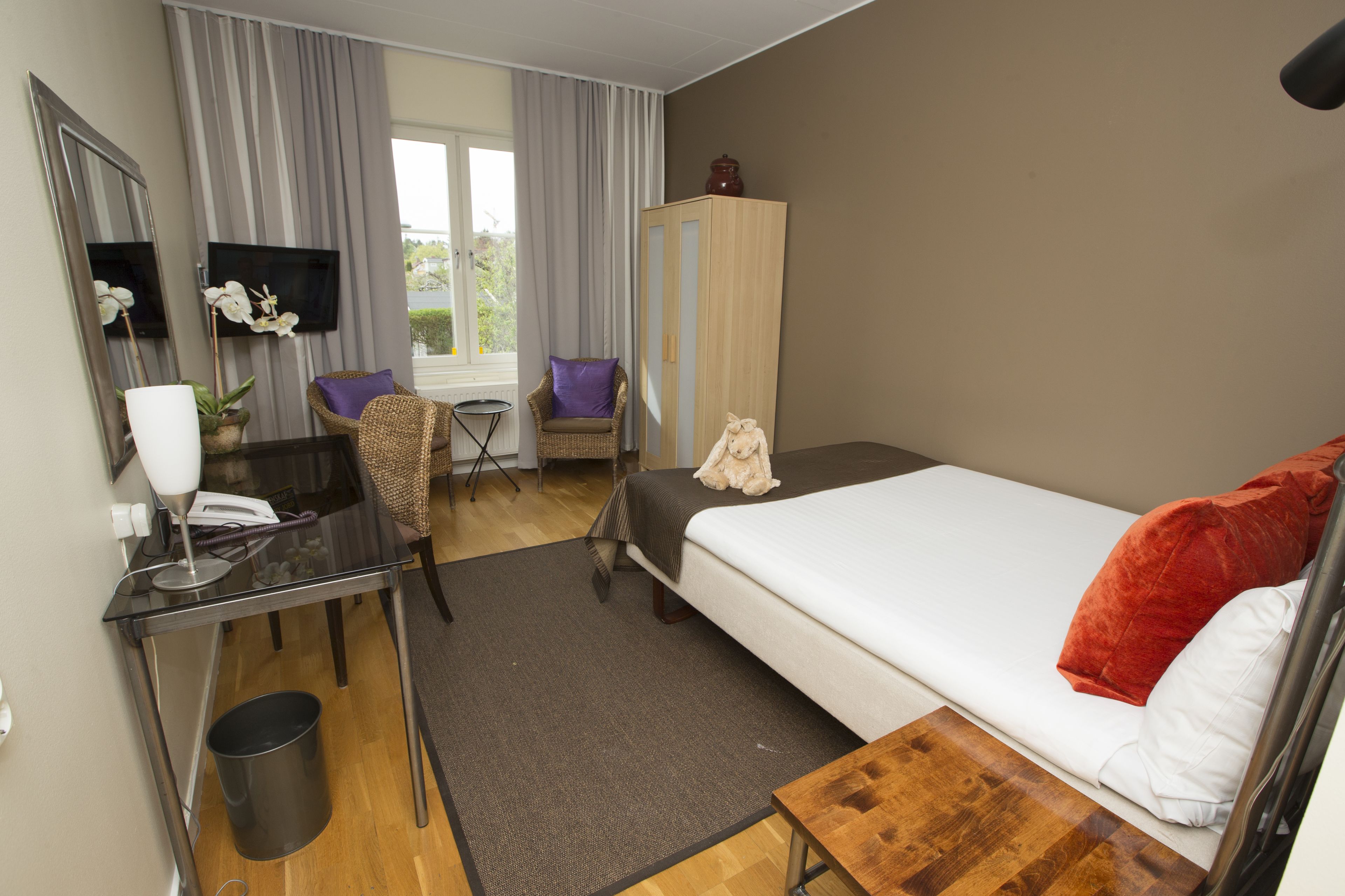 Habitació d'hotel amb llit, escriptori, cadira, televisió i finestra amb cortines.