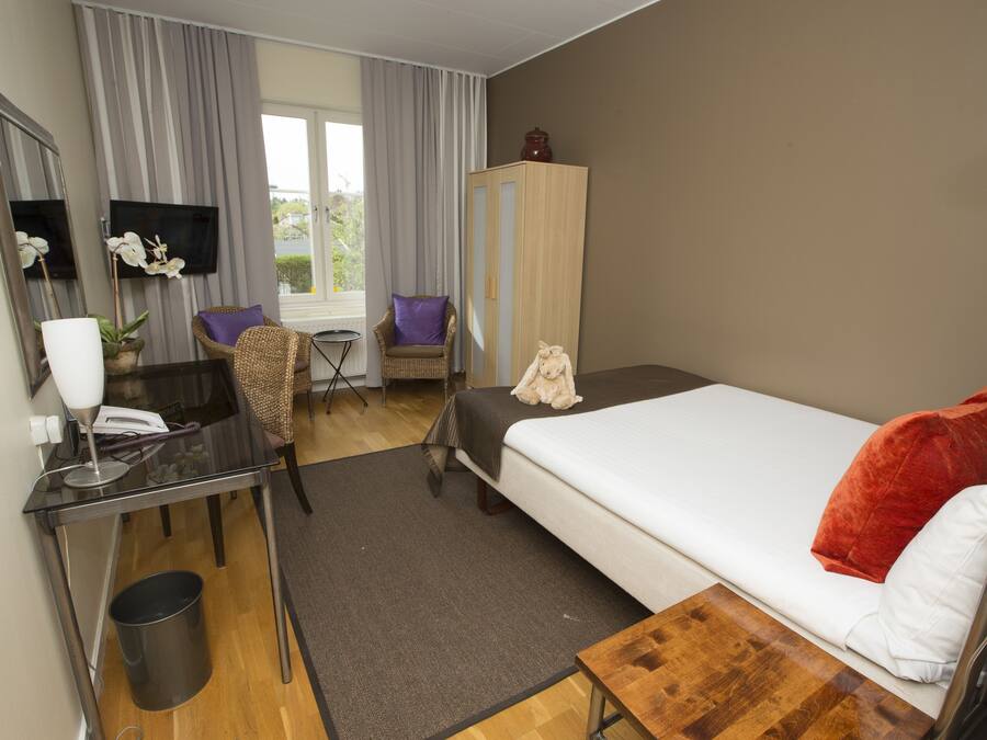 Habitació d'hotel amb llit, escriptori, cadira, televisió i finestra amb cortines.