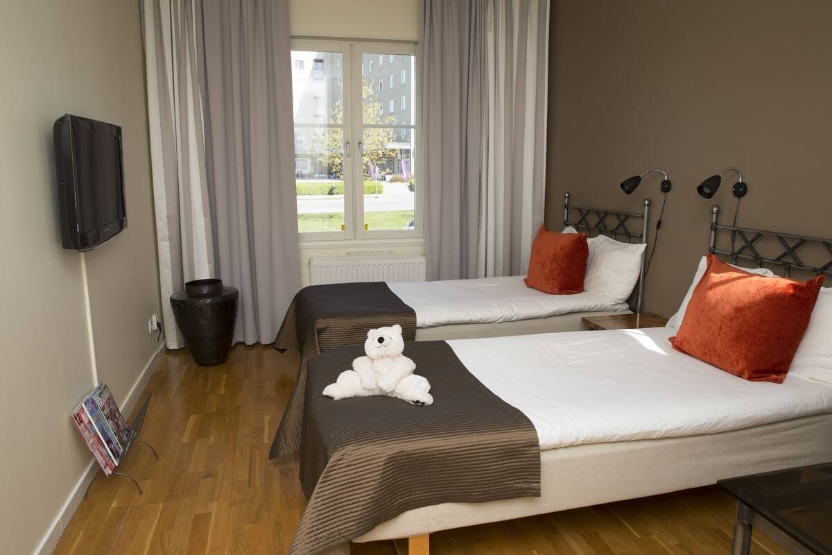 A hotel room with two beds, a TV, a window with curtains, and a wooden floor.